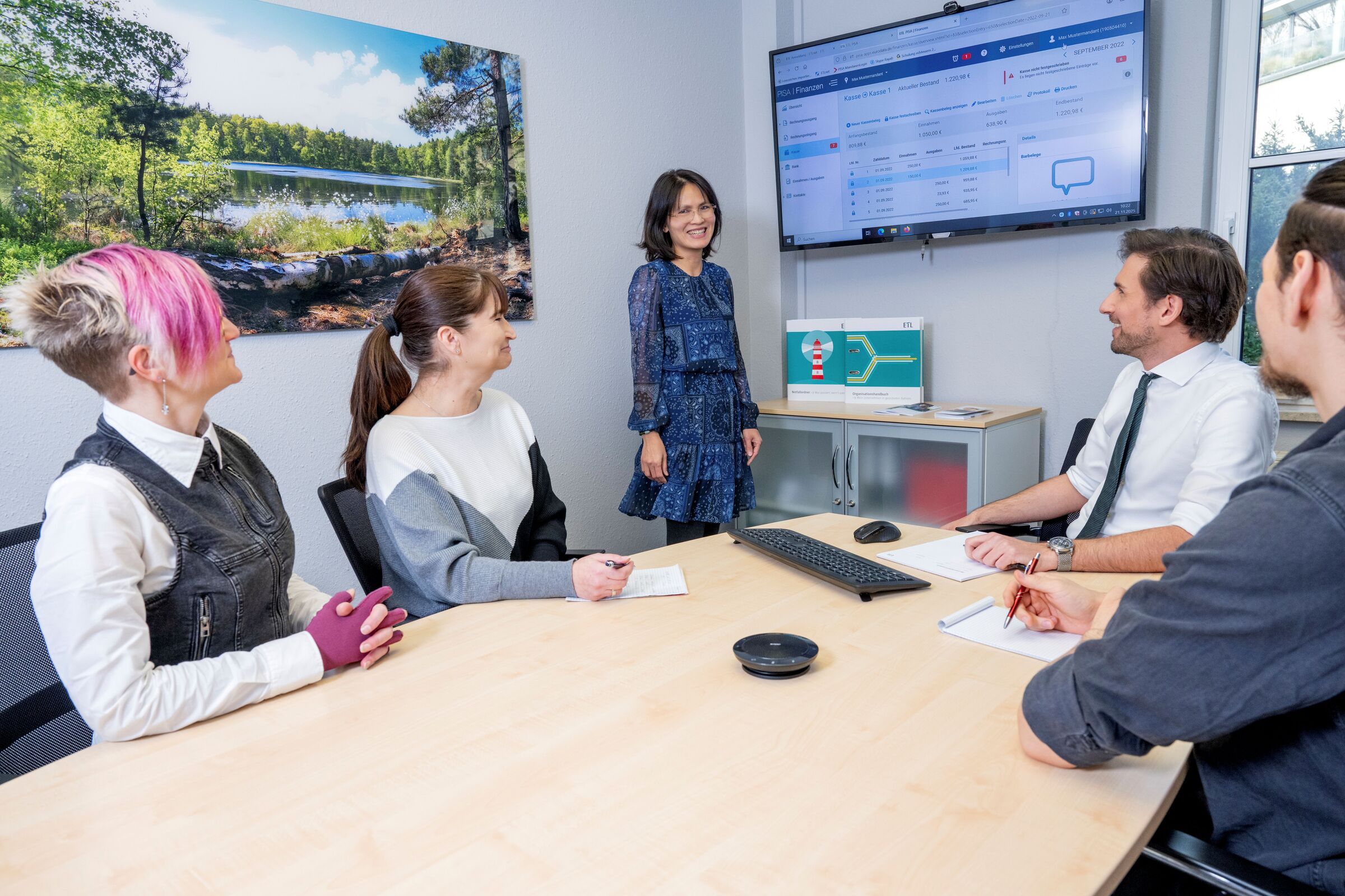 Mitarbeitende sitzen an einem Besprechsungstisch und hören einer Vortragenden zu